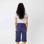 Rear view of a Female model wearing a white t-shirt and Wisdom of age canvas carpenter shorts in purple color on a light gray background
