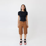 Female model wearing a black t-shirt and Wisdom of age canvas carpenter shorts in brick color on a light gray background