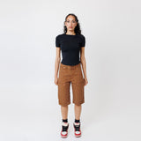 Female model wearing a black t-shirt and Wisdom of age canvas carpenter shorts in brick color on a light gray background