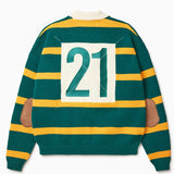 Rear View of the Wisdom of age Lemon rugby. This is a Green garment with yellow stripes, a cream collar. There is a embroidered number 21 within a cream box on the middle of the back and brown suede elbow patches on each sleeve.
