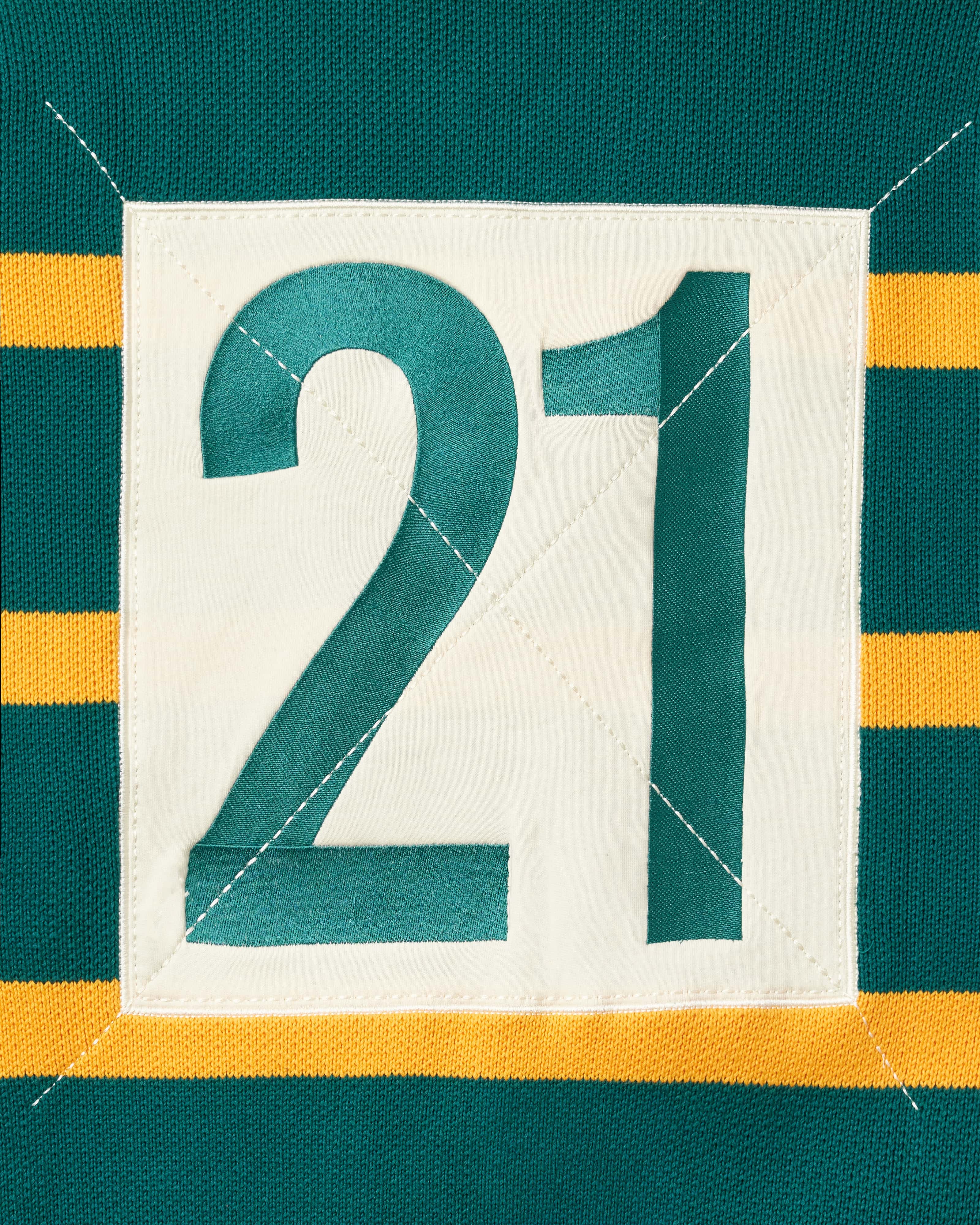 Close up of the number 21 within a cream box on the back of the WOA knit rugby polo.
