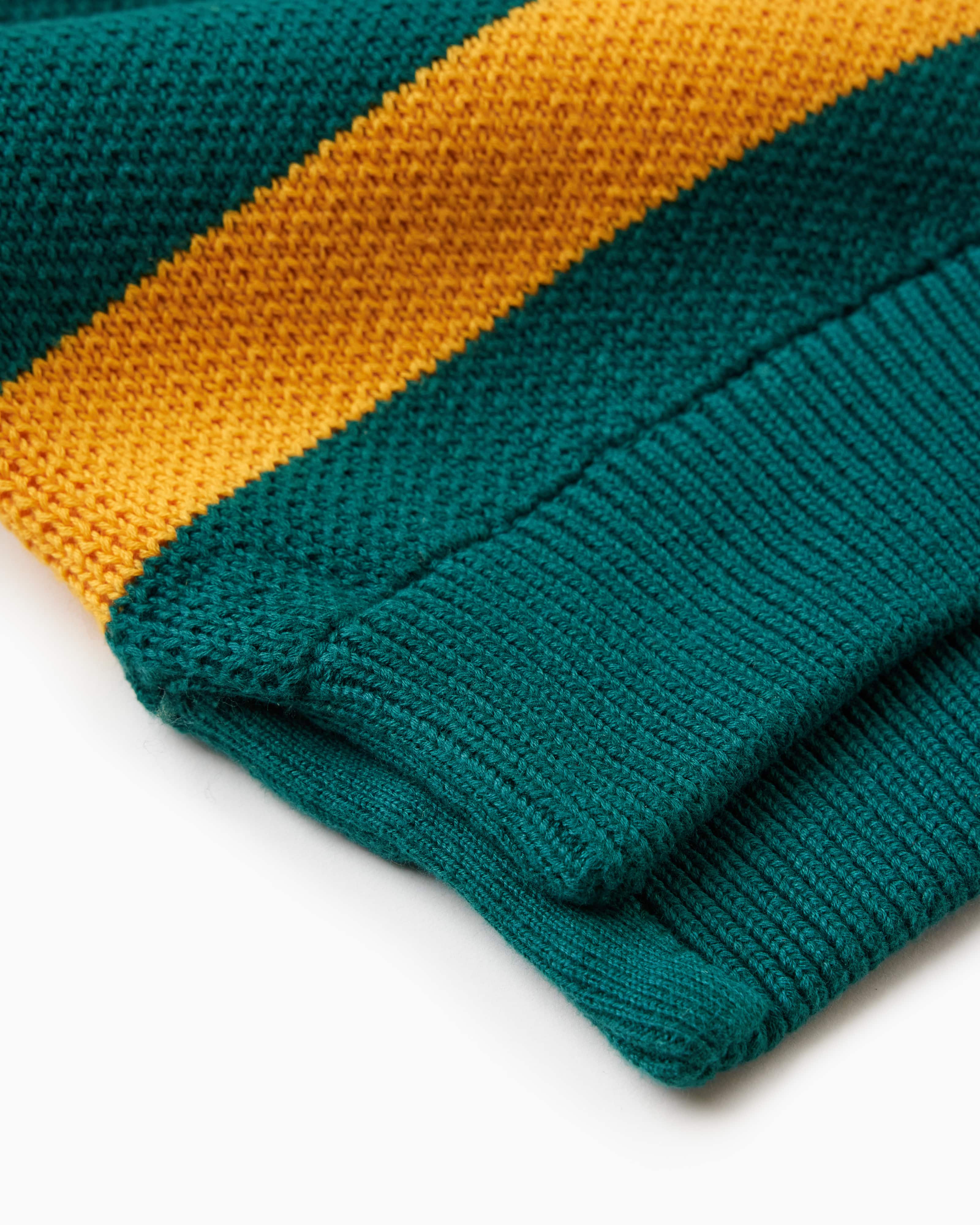 Close up of the bottom of the WOA knit rugby polo. Green polo with a yellow stripe.