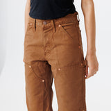 close up view of a Female model wearing a black t-shirt and Wisdom of age canvas carpenter shorts in brick color on a light gray background