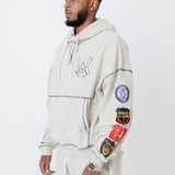 close up of a male model wearing a the W.O.A. Rugby Club Sweat suit in Sandstone with multiple embroidered patches on the sleeves and pant legs on a white background
