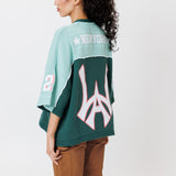 rear view of a female Model wearing a the WOA Football jersey V2 in the Mint color with 'Wisdom Of Age' and number '21' embroidered on the front. Model is wearing the WOA canvas carpenter shorts on a white background.