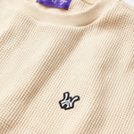 Close Front view of the Wisdom Of Age knit thermal shirt in cream. WA logo embroidered on the left chest in white with a black outline. Purple tag within the collar with Wisdom Of Age written in signature font.
