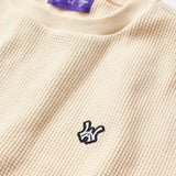 Close Front view of the Wisdom Of Age knit thermal shirt in cream. WA logo embroidered on the left chest in white with a black outline. Purple tag within the collar with Wisdom Of Age written in signature font.