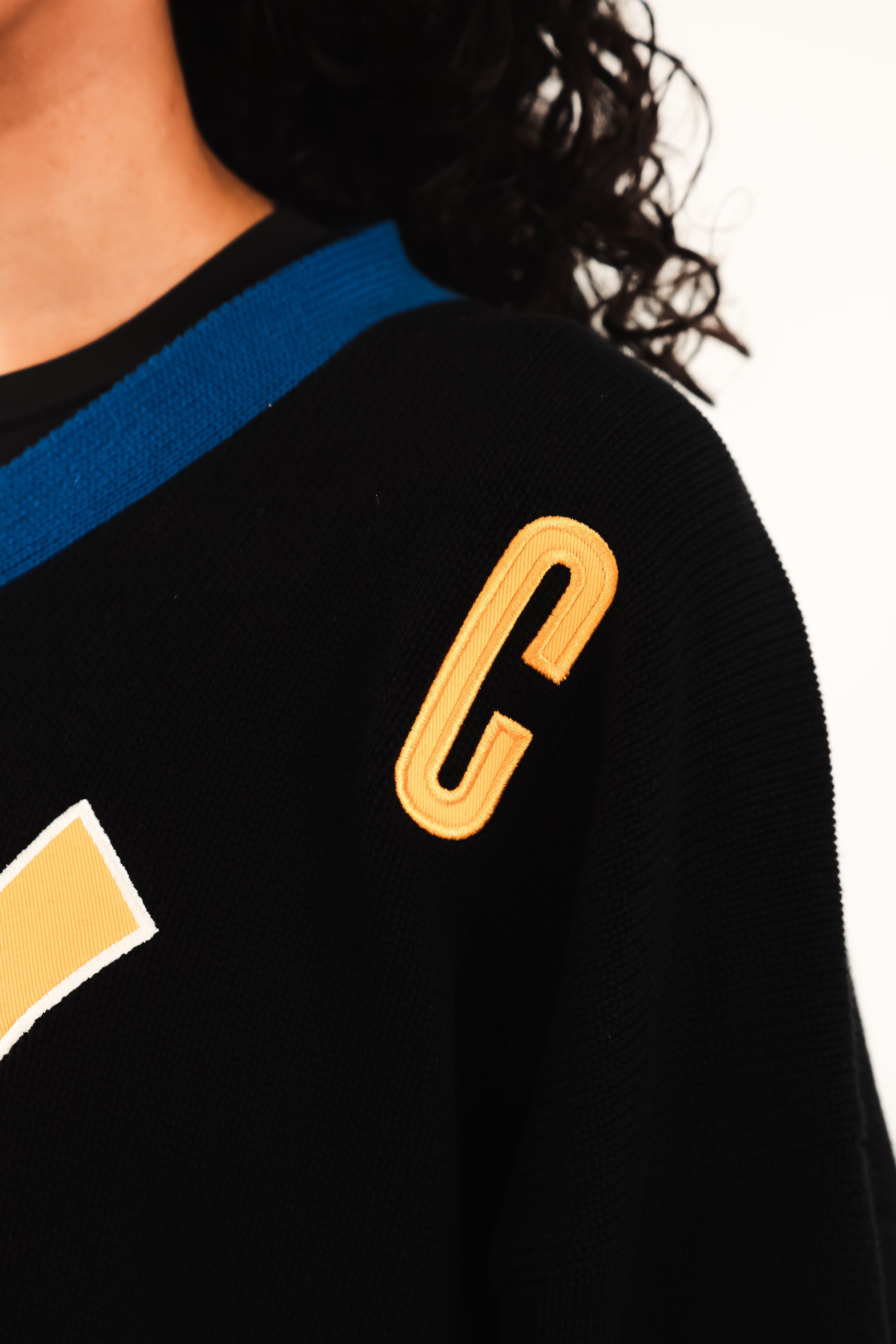 Close up on the WOA Knitted Hockey Jersey Static Shock with gold letter 'C' on a white background