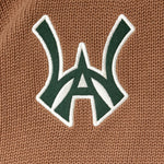 Close-up of a green WA logo with white outline on a brown textured background