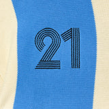 Close-up of the Wisdom Of Age Knit Soccer Jersey Celeste. A knitted soccer jersey with number 21 on a blue and beige background