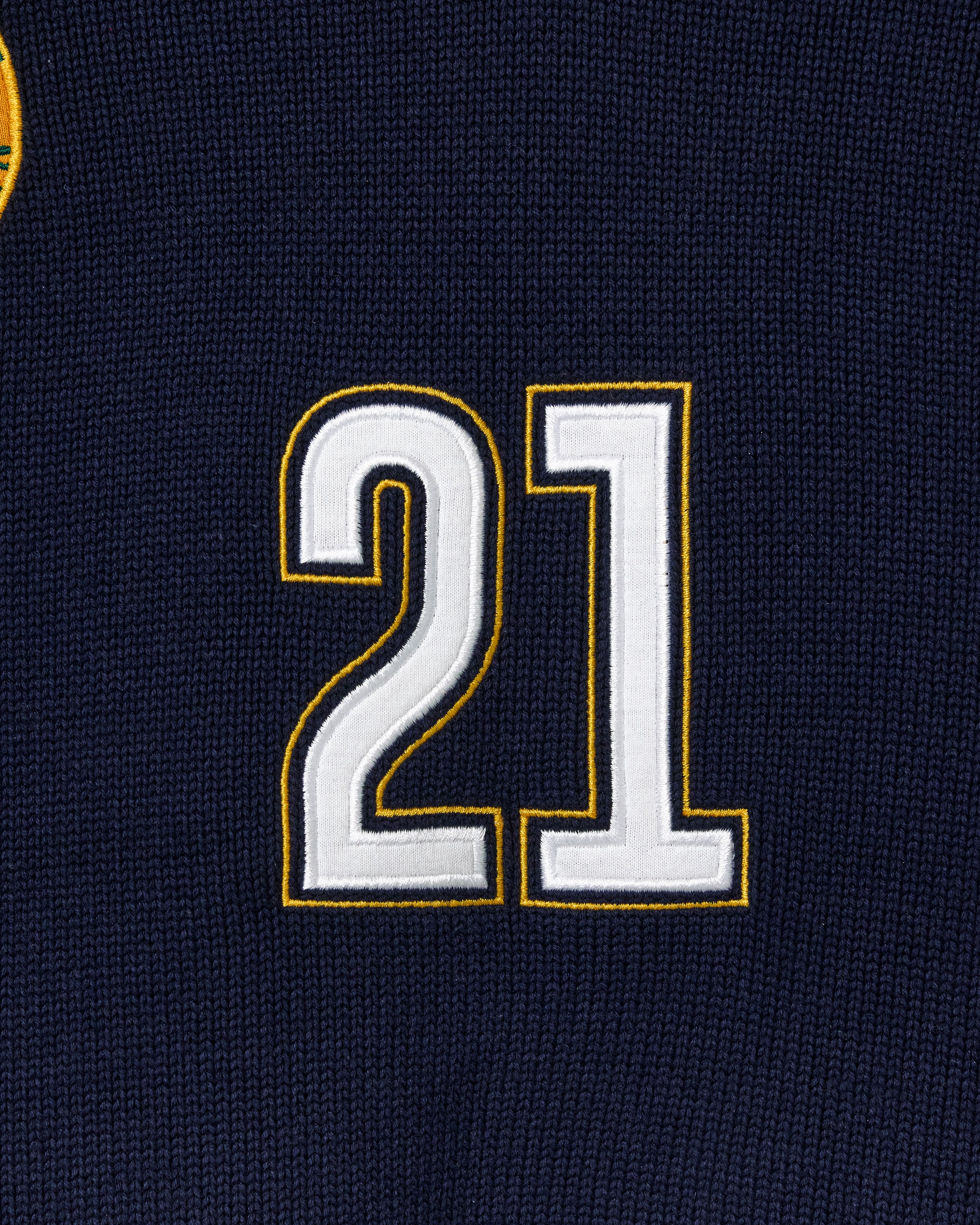 Close-up of a black knitted soccer jersey with the number 21 embroidered in white and gold.
