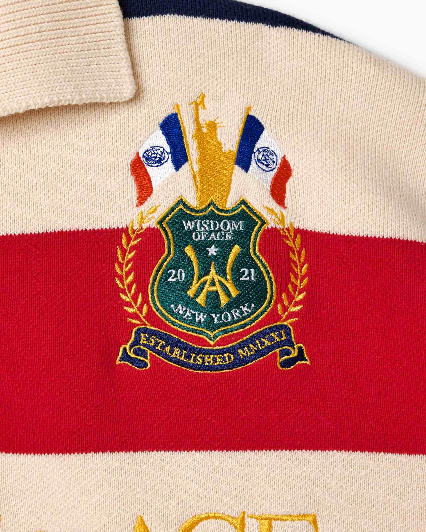 Wisdom of Age Bleecker Rugby Polo in multicolor stripes zoomed front view of embroidered ornate brand emblem .